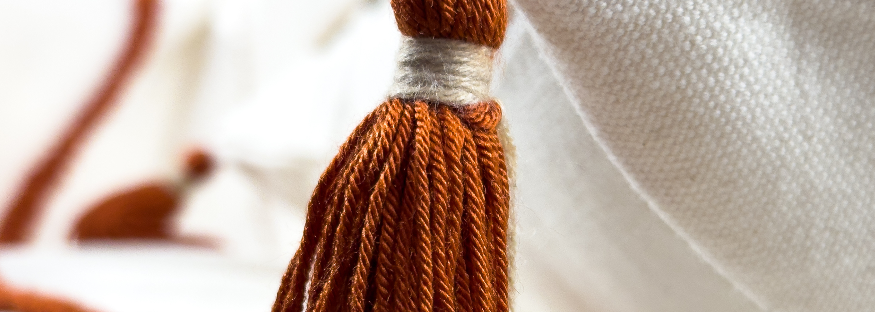 Close-up of a rust-colored tassel with a cream-colored band, set against a blurred white background.